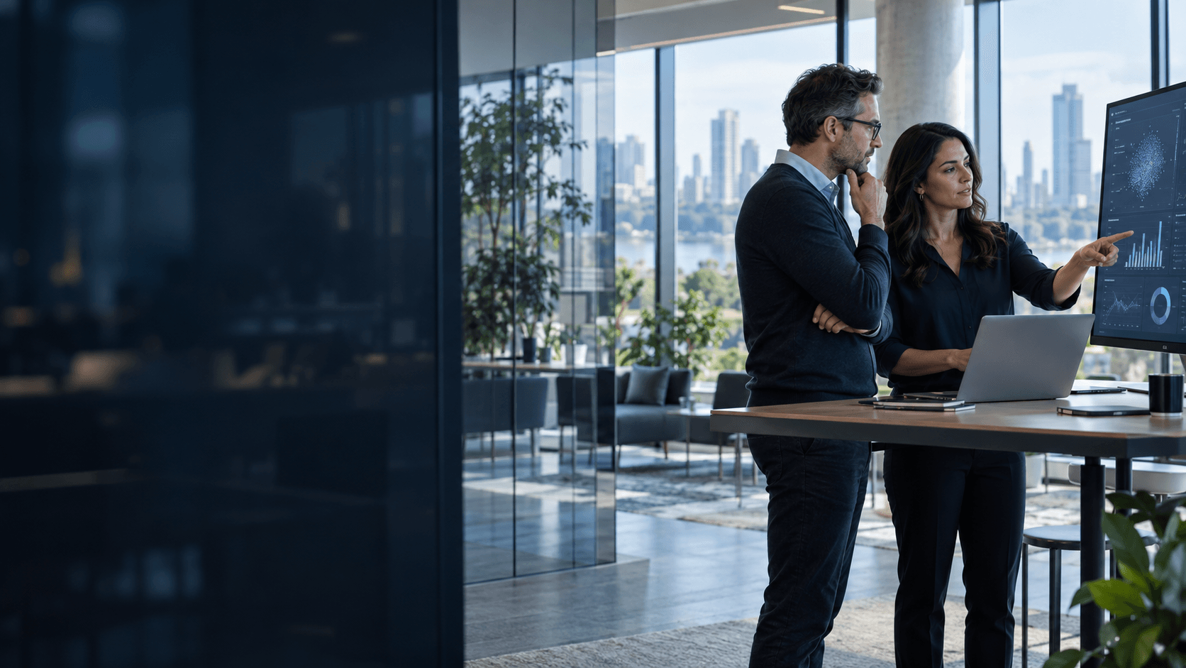 Two professionals review data visualizations in an engineering studio with large windows